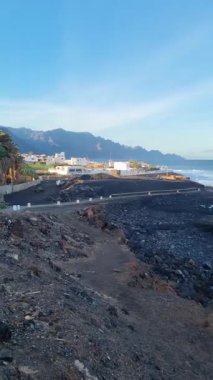 Sahilde kayalık arazi boyunca uzanan Puerto de las Nieves manzarası sahile vuran sakin dalgalar ve arka planda resim gibi dağlar. Göz kamaştırıcı doğal manzaralı sakin bir sahil köyü..