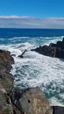 Charco del Viento, Tenerifes sahil güzelliği. Dalgalar açık mavi gökyüzünün altında volkanik kayalara çarpar ve dramatik ve vahşi bir okyanus manzarası yaratır..