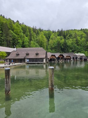 Bakir bir gölün sakin kıyıları boyunca büyüleyici kayıkhaneler, yemyeşil, yemyeşil bir manzarayla çevrili dağlarla çevrili..