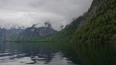 Berchtesgaden 'deki Bavyera Alpleri' nin yüksek uçurumları ve orman yamaçlarıyla çevrili Koenigssee Gölü 'nün durgun sularında sessiz bir tekne süzülüyor.