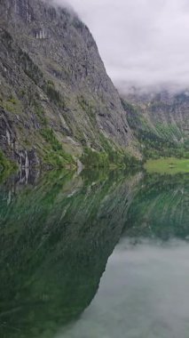 Obersee Gölü, Bavyera Alpleri 'ndeki alp kayalıklarını ve yeşil yamaçları yansıtır. Ormanlık dağlar ve bulutlu gökyüzü tarafından çerçevelenmiş uzak, kristal berraklığında su.
