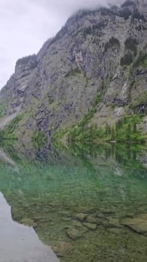 Knigssee kıyı şeridi su altındaki kayaların bozulmamış, cam gibi sularda olduğunu gösteriyor. Berchtesgaden Ulusal Parkı, Yukarı Bavyera 'daki sakin göl yükselen tepeleri yansıtır..