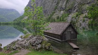 Berchtesgaden Ulusal Parkı, Bavyera, Almanya 'da şeffaf alp suyu ve dramatik dağ zeminiyle Obersee Gölü kıyısındaki Rustik ahşap kayıkhane.