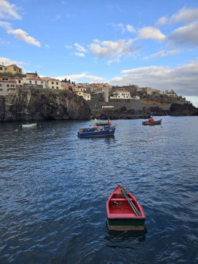 Cmara de Lobos, Madeira 'nın çarpıcı kıyı manzarası. Balıkçı tekneleri körfezi işaretlerken, canlı evler bu zamansız Portekiz köyünde kayalıklara tutunuyor..