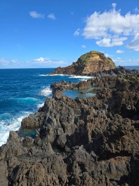 Porto Moniz, Madeira, Portekiz 'deki doğal volkanik havuzlar. Köpüklü Atlantik dalgaları, engebeli kuzey sahillerindeki dramatik bulutların altında karanlık lav kayalarına çarpar..