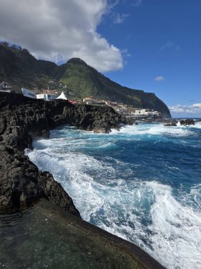 Porto Moniz, Madeira, Portekiz 'deki volkanik kayalara canlı Atlantik dalgaları çarpar. Doğal lav havuzları, kıyı köyleri ve masmavi gökyüzünün altındaki yemyeşil dağlar..