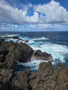 Dalgalar Portekiz, Madeira 'daki Porto Moniz doğal havuzlarında volkanik kaya oluşumlarına çarpar. Engebeli lav kıyıları ve mavi Atlantik dramatik doğal güzellikler yaratır..