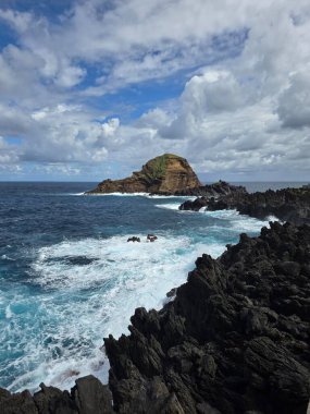 Dalgalar Portekiz, Madeira 'daki Porto Moniz doğal havuzlarında volkanik kaya oluşumlarına çarpar. Engebeli lav kıyıları ve mavi Atlantik dramatik doğal güzellikler yaratır..