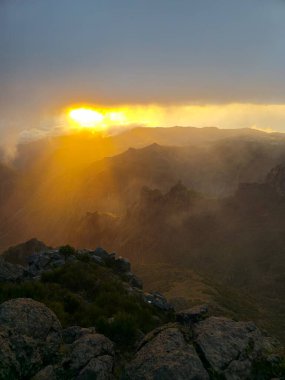 Pico do Arieiro 'da bulutların üzerinde, altın ışınlar zirvede dans ederek Madeiras dağlarının kalbinde huzurlu, rüya gibi bir atmosfer yaratıyor..