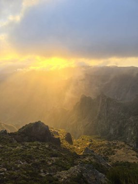 Bulutların üzerinde, Pico do Arieiro altın günışığıyla güneşleniyor, zirvelerden yükselen yumuşak bir sis ve dağları sıcaklıkla ve sükunetle saran sakin bir gökyüzü..