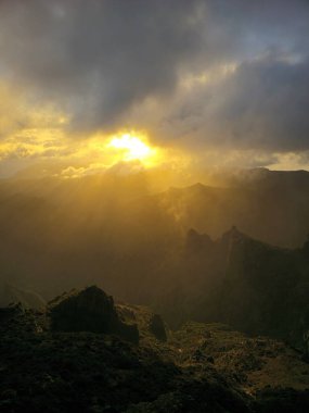 Pico do Arieiro, bulutların arasından kırılan, sisli tepeleri ısıtan ve Madeira 'nın üstündeki gökyüzünü altın renklerle boyayan yumuşak güneş ışınları altında parlıyor..