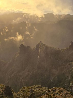 Pico do Arieiro 'da bulutların arasından güneş ışığı akar. Pürüzlü tepelerin üzerine sıcaklık saçar ve dağ havasını altın ve sakin enerjiyle doldurur..