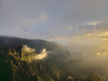 Altın ışınlar Pico do Arieiro 'da serin havayı ısıtıyor, bulutların arasında yavaşça parlıyor ve etrafındaki tepeleri yumuşak ışıkla yıkıyor, huzur ve merak uyandırıyor..