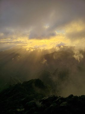 Pico do Arieiro 'nun üzerinde yoğun bulutların arasından geçen güneş ışınları Madeira' nın engebeli dağ sırasını gerçeküstü, rüya gibi bir sabah sahnesiyle aydınlatıyor..