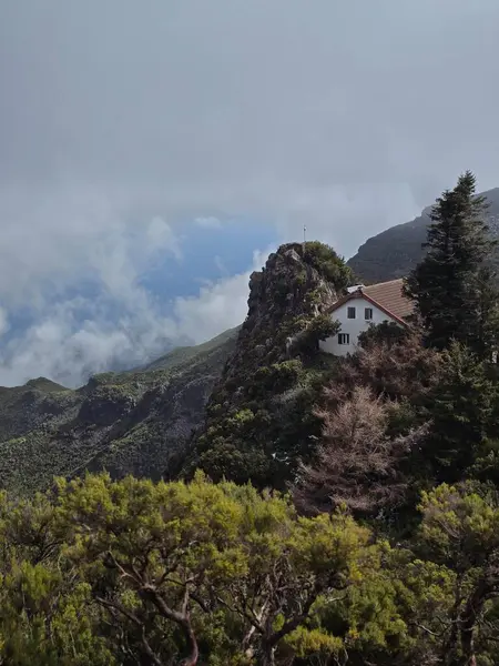 Pico Ruivo 'nun engebeli tepeleri arasında bulutlar sürükleniyor. Uzaktaki küçük bir ev engin dağlık araziyi demirliyor..