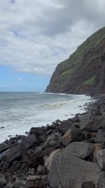 Dalgalar Madeiras 'ın kuzey kıyısındaki yüksek yeşil kayalıkların altındaki kayalık kıyıya çarpar. Erozyon ve vahşi volkanik güçler tarafından şekillendirilmiş dramatik bir Atlantik sahnesi.