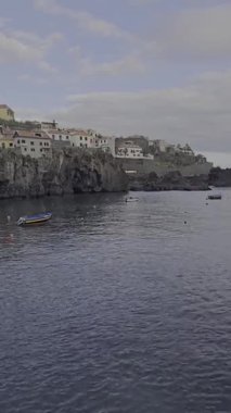 Geleneksel balıkçı tekneleri Cmara de Lobos, Madeira körfezinde yüzerler. Renkli yamaç evleri bu ikonik Portekiz kıyı köyünün kayalıklarını taçlandırıyor..