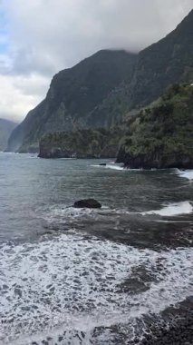 Portekiz 'in Madeira kentinin kuzey kıyısındaki Atlantik Okyanusu' na dramatik sahil kayalıkları düşer. Yeşilli yeşil yamaçlar, Vicente yakınlarında bulutlu bir gökyüzünün altında sakin denizle buluşuyor..