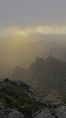 Pico do Arieiro üzerindeki bulutları delip geçen güneş ışınları kayalık tepelere altın ışık saçıyor. Sıcak ve huzurlu bir atmosferi olan huzur verici bir dağ manzarası..
