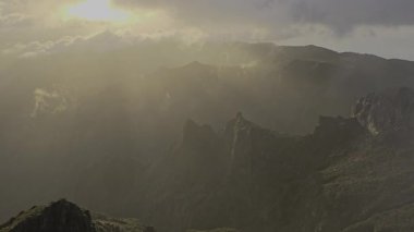 Pico do Arieiro üzerinde kalın bulutların arasından geçen altın ışınlar. Dağ zirveleri sabah sıcaklığıyla parlıyor, Madeira 'da dünya üzerinde barışçıl bir başlangıç sunuyor..