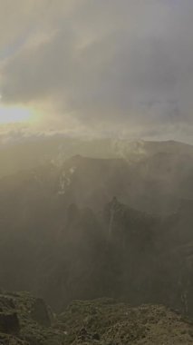 Pico do Arieiro üzerinde bulutların arasından güneş ışınları çıkıyor, dramatik tepelere altın ışık saçıyor.. 