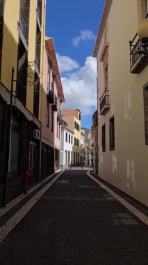 Renkli koloni binaları, Portekiz, Madeira, Funchal 'da sessiz bir kaldırım hattı oluşturur. Parlak bir Atlantik gökyüzünün altında güneşli bir sokak..
