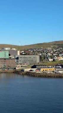 Trshavn, Faroe Adaları 'nın modern rıhtımı, cam ofisleri ve liman duvarlarıyla, bulutsuz Kuzey Atlantik yaz gökyüzü altında rüzgar türbinleri ile kaplı yeşil tepelere karşı kuruludur..