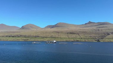 Korunaklı Faroe Adaları körfezindeki bazalt kayalıklara karşı modern somon balığı yuvaları, bulutsuz bir günde sürdürülebilir Kuzey Atlantik deniz ürünleri yetiştirildiğini göstermektedir.