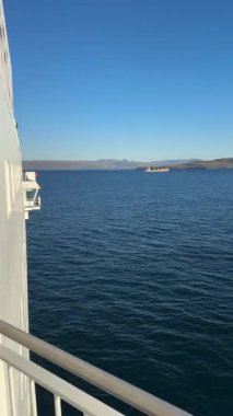 Faroe Adaları yakınlarındaki Kuzey Atlantik üzerinde bir feribot görüntüsü. Bir gemi parlak mavi gökyüzü ve sakin denizin altında kayalık adaların yanından geçiyor..