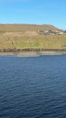 Açık bir günde Faroe Adaları 'nın kayalık kıyı şeridi boyunca somon çiftliği kafesleri ve bir tekne. Saf İskandinav deniz manzarasında sürdürülebilir su kültürü.