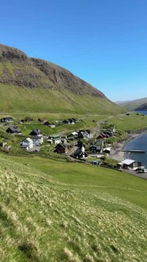 Faroe Adaları, Vgar Adası 'ndaki Bour' un resimli sahil köyü. Geleneksel İskandinav evleri, yeşil tepeler ve berrak mavi gökyüzünün altında büyüleyici fiyort manzaraları..