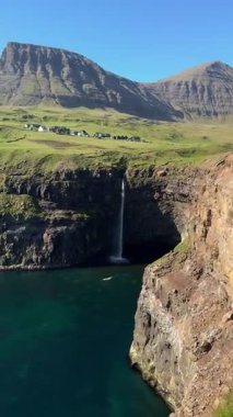 Mlafossur Şelalesi, Gsadalur köyünün kayalıklarından, Faroe Adaları 'ndaki Vgar Adası' ndaki Atlantik Okyanusu 'na, açık bir yaz gökyüzü altında düşer..