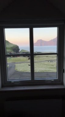 Faroe köyüne bakan bir pencereden, virajlı bir yoldan ve gün batımında uzak bir dağdan. Faroe Adaları 'ndaki huzurlu kırsal manzara.