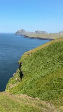 İzlanda, Vestmannaeyjar 'dan kıyı manzarasını tarıyorum. Yeşil kayalıklar Atlantik Okyanusu 'na dökülüyor. Parlak mavi gökyüzünün altındaki uzak adalar. Sakin ve vahşi bir ufuk..