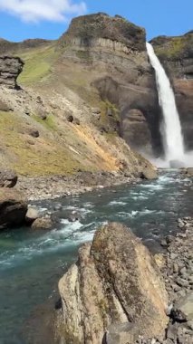 Hifoss şelalesi İzlanda 'daki Hekla volkanı yakınlarındaki kayalık bir kanyona düşer. Ham kayalıklar ve volkanik araziler tarafından çerçevelenmiş buzul suları ön planda akar..