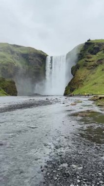 İzlanda 'da Skgafoss gök gürültülü bir güçle yeşil kayalıklar ve sabit sis ile çevrili kayalık bir ovaya daldı..