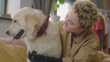 Protez kollu, neşeli genç bir kadın oturma odasındaki kanepede köpeğini okşayıp kucaklıyor.