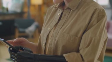 Protez kollu bir kızın evde dikilip akıllı telefon kullandığı seçmeli bir odak noktası.