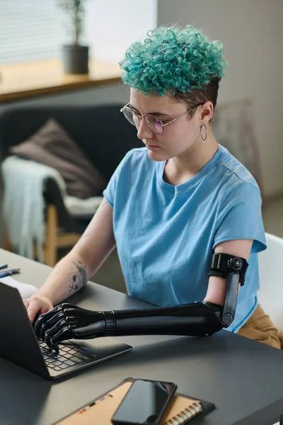 Young woman with prosthetic arm concentrating on her online work on laptop, she working at home