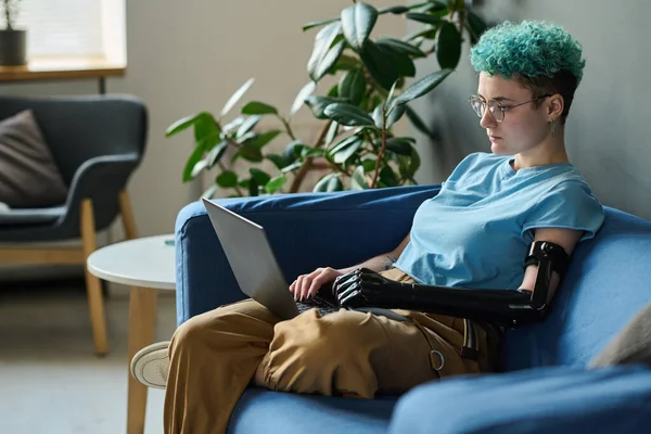 Engelli bir kadın kanepede oturuyor ve dizüstü bilgisayar kullanıyor. Boş zamanlarında internetten iletişim kuruyor.