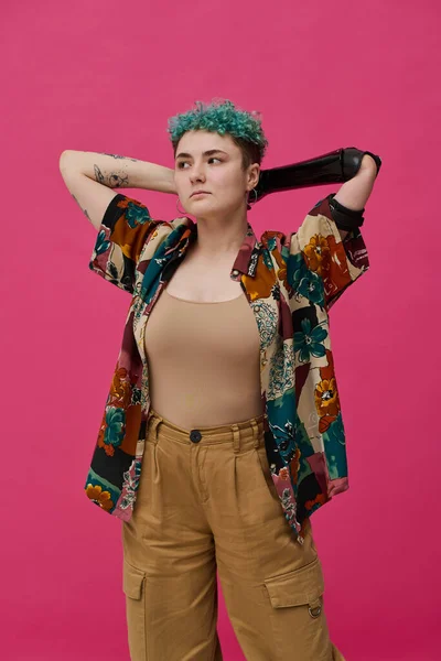 Portrait of young woman with prosthetic arm in stylish clothing posing against pink background