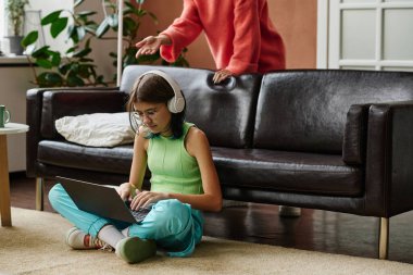 Ergen, dizüstü bilgisayarda oyun oynarken annem ona bir şey söylüyor.