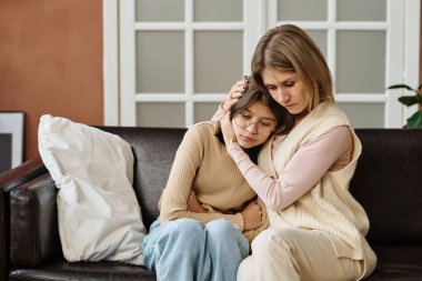 Anne kızıyla birlikte kanepede oturuyor ve onu kucaklıyor, depresyon sırasında onu rahatlatıyor.