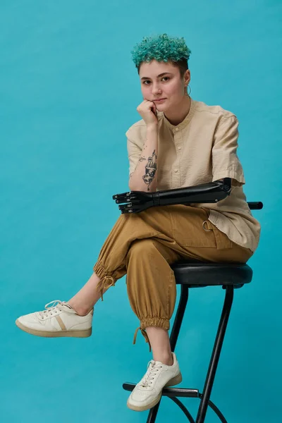 Retrato Adolescente Com Braço Protético Posando Cadeira Contra Fundo Azul — Fotografia de Stock