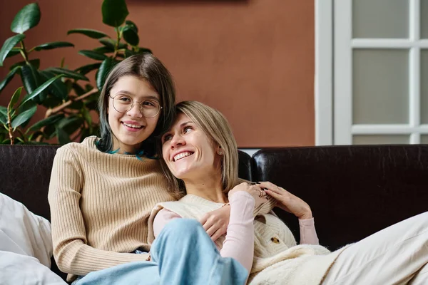 stock image Happy teenage girl embracing her mother and smiling while they resting on sofa in the room