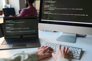 Bilgisayar programı için kod yazan programcıya yakın plan, o bilgisayar monitörüyle masada oturuyor