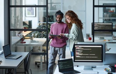 Dijital tablet kullanan genç meslektaşlar bilişim ofisinde bilgisayar programıyla çalışıyorlar.