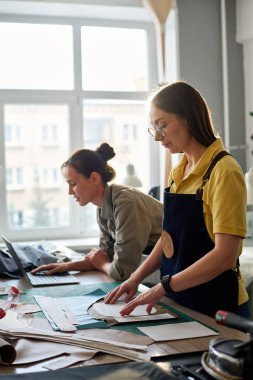 Atletizm ya da moda atölyesinde çalışan kadın terzilerin yan görünüşü. Biri ağ kurarken diğeri de dikiş desenlerini daire içine alacak.