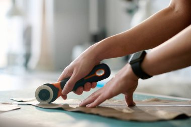 Keskin bıçaklı genç kadın tabakçının elleri, yeni bir parçayı dikmeden önce, deri parçasının ana hatlarını kesiyor.