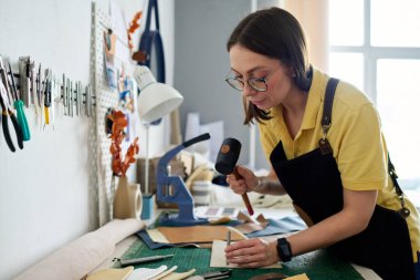 Deneyimli kadın deri işçisi çekiçle vururken deri ya da süet parçasına küçük çelik şaft bastırıyor.